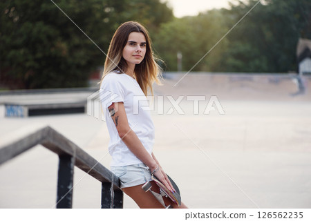 Young attractive girl in a white t-shirt and sneakers in modern skatepark with skateboard Young attractive girl in a white t-shirt and sneakers in modern skatepark with skateboard 126562235