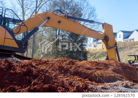 Heavy machinery performs excavation at construction site as homes overlook work area Heavy machinery performs excavation at construction site as homes overlook work area 126562570