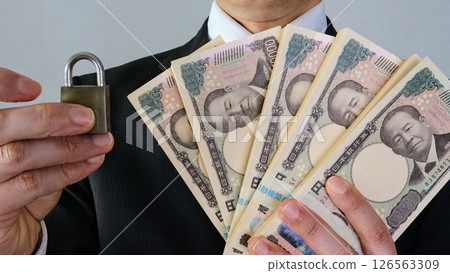 Businessman holding a stack of bills and a padlock Businessman holding a stack of bills and a padlock 126563309