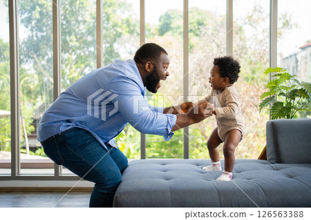 Portrait Of Happy African American Dad With Cute Little Baby Girl on couch at home in the living room, caring father smiling and amusing his girl while sitting on the couch, happy family Portrait Of Happy African American Dad With Cute Little Baby Girl on couch at home in the living room, caring father smiling and amusing his girl while sitting on the couch, happy family 126563388