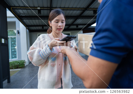 Cheerful Asian women receive product box from delivery service and pays by scanning QR code from smartphone, home deliveries, a convenient shopping experience, and trustworthy doorstep service concept 126563982
