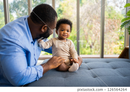 Portrait Of Happy African American Dad With Cute Little Baby Girl on couch at home in the living room, caring father smiling and amusing his girl while sitting on the couch, happy family 126564264