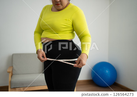 Overweight woman using a tape measure around waist and belly fat, Fat Asian woman workout at home. Concept of healthy, food for health and lifestyle, weight loss 126564273
