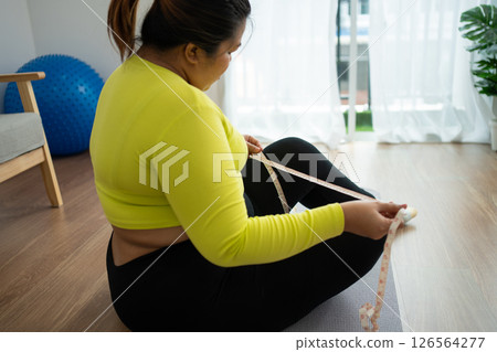 Overweight woman using a tape measure around waist and belly fat, Fat Asian woman workout at home. Concept of healthy, food for health and lifestyle, weight loss 126564277