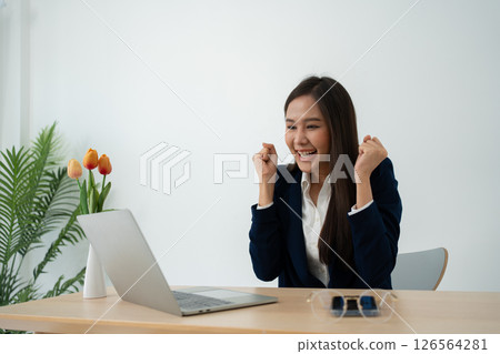 Portrait of a Young attractive Asian woman in a black business suit feeling euphoric celebration online win success achievement result. Success, win, victory, triumph, congratulation, concept. 126564281