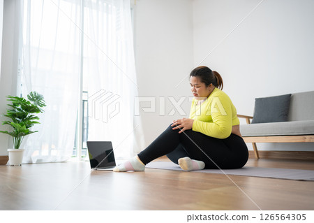 Unhappy plus size woman sitting on the floor, having knee pain during exercise, unable to exercise because of sports injury, feeling pain. Exercising properly concept, health care. weight loss 126564305