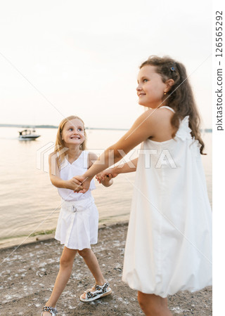 Young girls are playing on beach, one of them wearing white dress Young girls are playing on beach, one of them wearing white dress 126565292