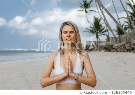 Harmony and meditation training during morning yoga at coastline beach, contemplative female in sportswear praying in namaste pose 126565446