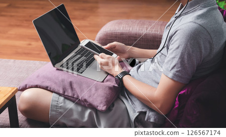 A man in casual wear using smartphone and laptop while he is working at home office. 126567174