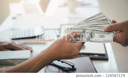 Man offering batch of hundred dollar bills. Hand of a businessman giving money to his partner. Hand receiving money from businessman. Venality, bribe, corruption concept. 126567179