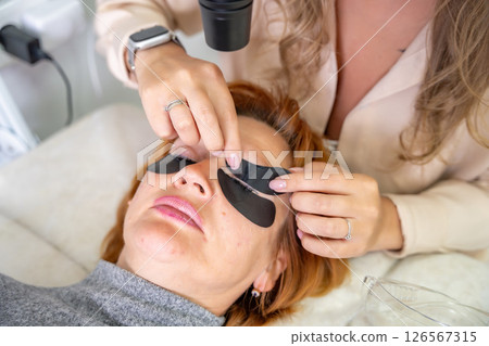 Beautician applying black eye patches before eyelash extension procedure with ultraviolet lamp. Innovative lash extension method in modern beauty salon 126567315