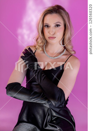 An Elegant Fashion Model Dressed in a Glamorous Black Attire Set Against a Pink Background 126568320