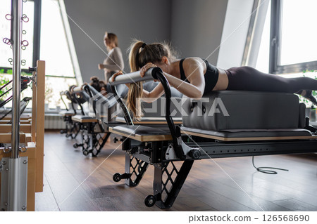 Womens doing Swan exercise on Pilates Reformer for the chest and back muscles, focusing on flexibility, strength, and control with determination 126568690