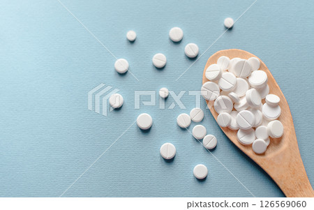 Close-up white pills, tablets in wooden spoon on blue table. Medicine and health concept. pharmaceutics. Top view. Pills and vitamins 126569060