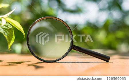 Close up Single Magnifying Glass with Black Handle, Leaning on the Wooden Table on outdoors. 126569063
