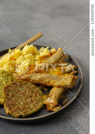 A wholesome breakfast featuring turmeric rice with baked ocean fish, complemented by broccoli pancakes and roasted vegetables, offering a nutritious and satisfying meal A wholesome breakfast featuring turmeric rice with baked ocean fish, complemented by broccoli pancakes and roasted vegetables, offering a nutritious and satisfying meal 126569700