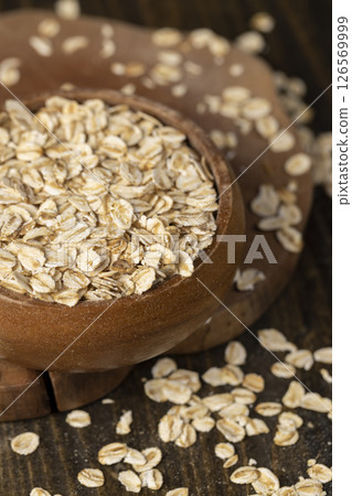 bowl with oatmeal flakes for making porridge, scattered dry cereal flakes from oats flattened and steamed, closeup, side view 126569999