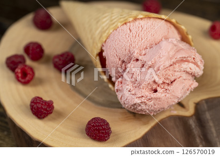 pink sweet raspberry-flavored ice cream lies on a walnut board, ripe red raspberries and raspberry cold natural ice cream on the table, close up pink sweet raspberry-flavored ice cream lies on a walnut board, ripe red raspberries and raspberry cold natural ice cream on the table, close up 126570019