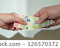 Female and male hands holding or handing over a bundle of euros. Financial transaction. 126570372