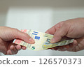 Female and male hands holding or handing over a bundle of euros. Financial transaction. 126570373