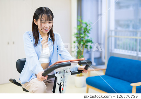 Woman exercising on a fitness bike in her home room, home, exercise bike, exercise Woman exercising on a fitness bike in her home room, home, exercise bike, exercise 126570759