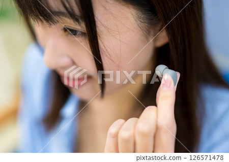 A woman picking up commercially available wireless earphones 126571478