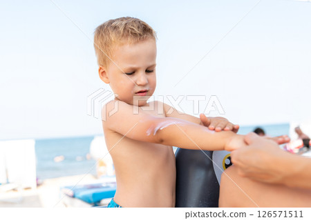 Mother applying sunscreen protection creme on cute little baby boy kid face. Mum using sunblocking lotion to protect baby from sun during summer sea vacation. Child healthcare travel vacation time 126571511