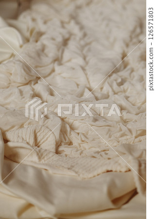 Close-up of wrinkled white fabric on bed in soft light Close-up of wrinkled white fabric on bed in soft light 126571803