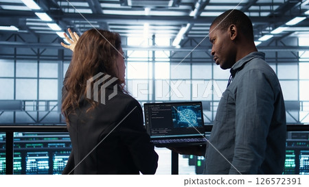 Software developers using AI tech on laptop in data center managing server virtualization. IT expert coding on notebook in server room using artificial intelligence, finetuning network, camera B 126572391