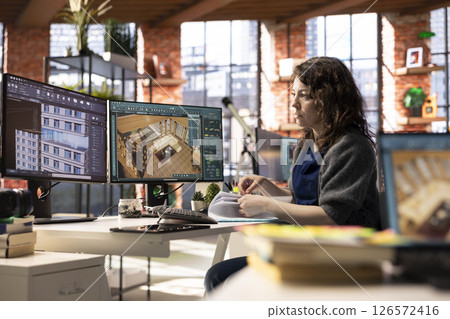 Freelancer designer decorates an apartment floor plan on a computer, using architectural software to configure elements. Woman uses interface to enable rendering and 3D modeling. Freelancer designer decorates an apartment floor plan on a computer, using architectural software to configure elements. Woman uses interface to enable rendering and 3D modeling. 126572416