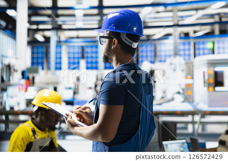 African american supervisor evaluates renewable energy metrics at factory, using advanced monitoring and manufacturing tools on files. Engineer improves solar power system accuracy. African american supervisor evaluates renewable energy metrics at factory, using advanced monitoring and manufacturing tools on files. Engineer improves solar power system accuracy. 126572429