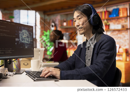 AI startup office chief technology officer listening music while building application. Senior developer wearing headphones while working in artificial intelligence software development agency 126572433