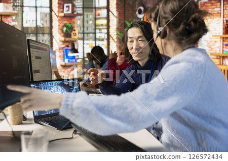 Smiling Asian call center onboarding specialist training new agent on helpful AI tools. Friendly senior manager in customer support department office shows woman how to use company AI software 126572434