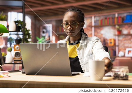 Teleworker using laptop device in apartment office to write emails. Remote employee in home workspace typing on notebook keyboard, composing documents in order to deliver project 126572456
