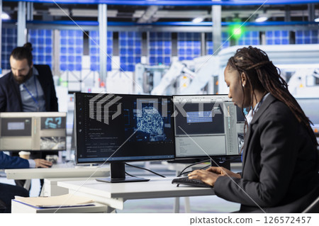 Factory worker writing AI code at workstation in photovoltaic plant, creating predictive maintenance tools. Engineer using artificial intelligence to analyze production patterns and do improvements 126572457