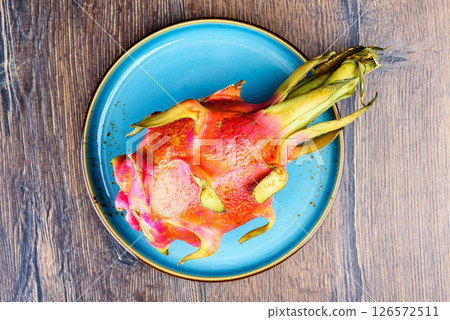 Top view of whole and ripe unpeeled pitahaya on blue plate. 126572511