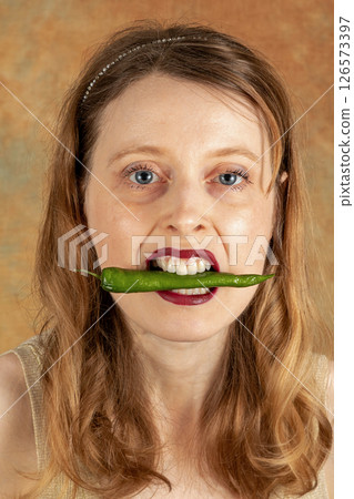 Holding green hot pepper in mouth 126573397