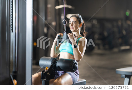 Fit woman performing lat pulldown on cable machine at gym Fit woman performing lat pulldown on cable machine at gym 126575751