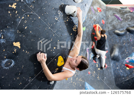 Female fitness climber training at bouldering gym. Young woman rise up on artificial climbing wall 126575768