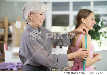 Mature tailoress measuring female client in sewing workshop 126575770