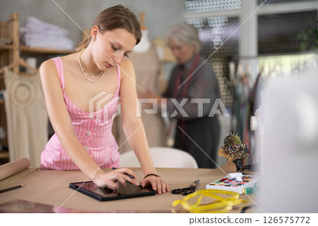 Young female dressmaker drawing in tablet other work with mannequin Young female dressmaker drawing in tablet other work with mannequin 126575772