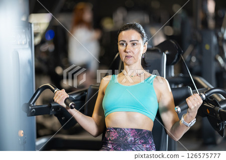 In gym, woman uses chest press machine to strengthen arm muscles In gym, woman uses chest press machine to strengthen arm muscles 126575777