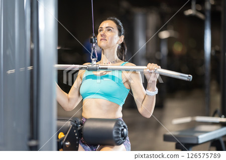 Woman performing wide-grip lat pulldown on cable machine at gym 126575789