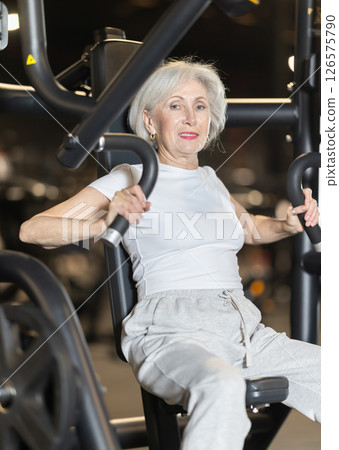 Elderly woman training on chest press machine in gym Elderly woman training on chest press machine in gym 126575790