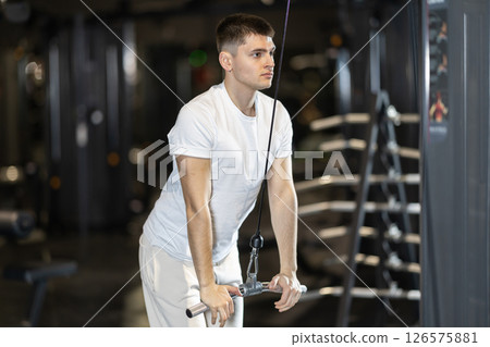 In gym, man uses cable row machine to strengthen muscles. In gym, man uses cable row machine to strengthen muscles. 126575881