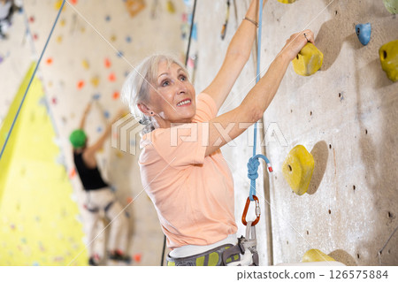 Determined senior woman doing her best at climbing artificial wall 126575884