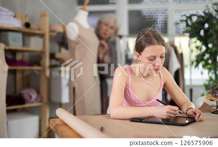 Young woman draws pattern on tablet female assistant sews on mannequin 126575906