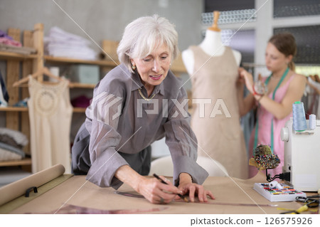 Mature tailor draws of a fashion design against the background of a assistant 126575926