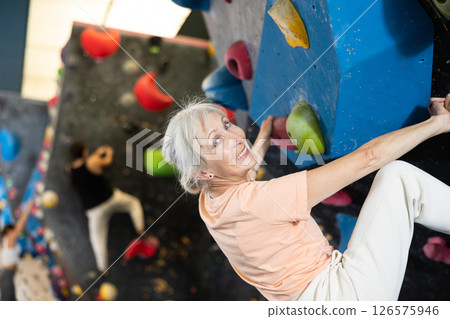 Mature female fitness climber training at bouldering gym.Woman rise up on artificial climbing wall Mature female fitness climber training at bouldering gym.Woman rise up on artificial climbing wall 126575946
