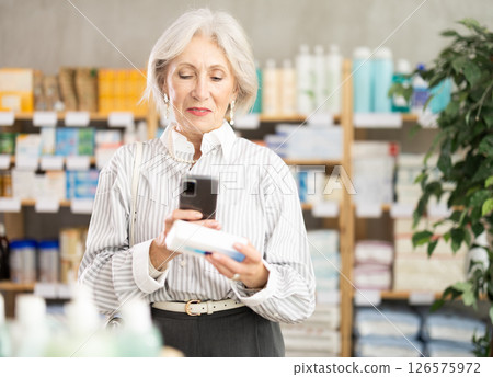 Elderly woman scans the barcode of a package of ointment 126575972